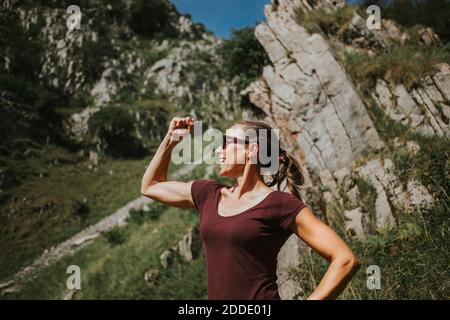 Femme souriante qui plie les muscles tout en se tenant contre la formation de roche jour ensoleillé Banque D'Images