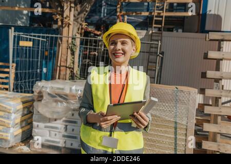 Femme souriante surveillant utilisant une tablette numérique tout en se tenant debout à la construction site Banque D'Images