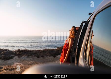 Young woman leaning on camper van at beach Banque D'Images
