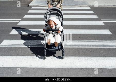 Mère avec son fils dans la rue de traversée de voiture de bébé dans la ville par beau temps Banque D'Images