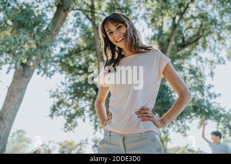 Femme mûre souriante avec main sur la hanche debout en public garez-vous par beau temps Banque D'Images
