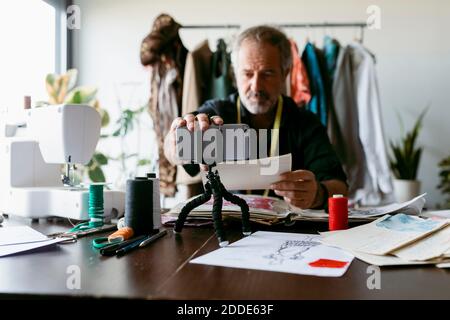 Homme mature adapter le smartphone sur trépied lors de l'enregistrement au studio de travail Banque D'Images