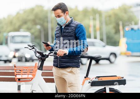 Jeune homme utilisant un téléphone portable tout en restant dans la rue Ville pendant COVID-19 Banque D'Images