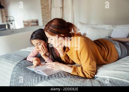 Mère et fille lisant le livre tout en étant allongé sur le lit à accueil Banque D'Images