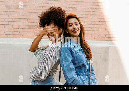 Ami couvrant l'œil avec la main tout en se tenant dos à dos avec la femme contre le mur Banque D'Images