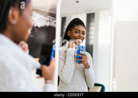Femme souriante prenant le selfie par réflexion de miroir à la maison Banque D'Images