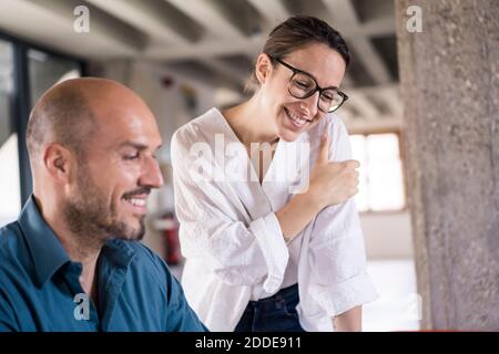 Femme d'affaires souriante debout près d'un homme au bureau Banque D'Images