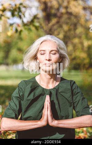 Femme assise avec les mains clastées en faisant du yoga au parc Banque D'Images