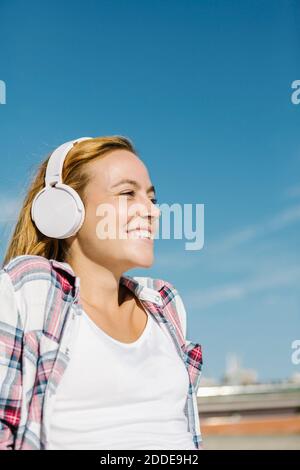 Bonne femme écoutant de la musique avec un casque, en regardant loin du bleu ciel le jour ensoleillé Banque D'Images