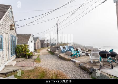 Chaises et barbecues devant des cabines en bois le long d'un sentier côtier couvert de brouillard matinal en automne Banque D'Images