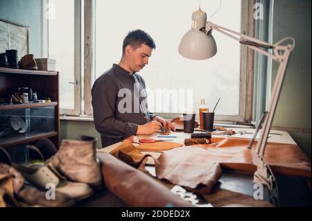 Un jeune cordonnier de la vieille école remplit un ordre de fabriquer un produit en cuir exclusif. Portrait en studio. Banque D'Images