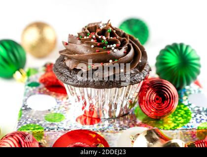 Un gâteau au chocolat de Noël est placé sur un cadeau de papier d'aluminium emballé avec des ornements de Noël dispersés autour. Arrière-plan blanc. Banque D'Images