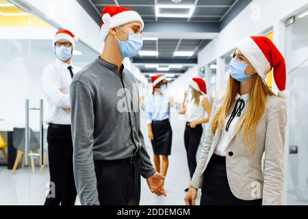 Équipe de gens d'affaires dans les masques de protection médicale sur les visages et les casquettes rouges du Père Noël communiquant dans le bureau, Noël, coronavirus, quaranti Banque D'Images