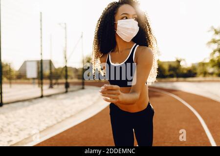 Belle afro-américaine femme dans un masque médical protecteur sur son visage, jogging à l'extérieur, fitness, les gens et un mode de vie sain Banque D'Images