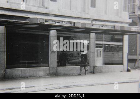 Belle photographie en noir et blanc vintage des années 1970 d'une femme marchant dans la rue. Banque D'Images