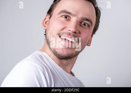 Beau gars de brunette avec des poils dans un T-shirt blanc fait grimaces amusants sur son visage Banque D'Images