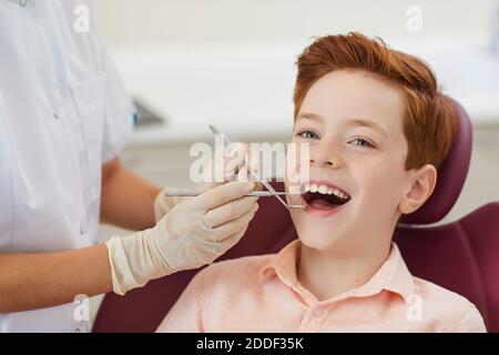 Clinique dentaire. Garçon souriant obtenant l'examen des dents de femme dentiste Banque D'Images