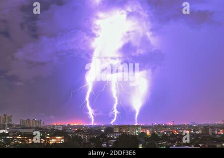 Tempête électrique montrant trois boulons éclairants frappant la terre sur un paysage urbain de nuit. Banque D'Images