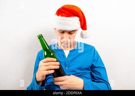 Sad Young Man à Santa Hat avec une bouteille de bière Près du mur dans la pièce Banque D'Images