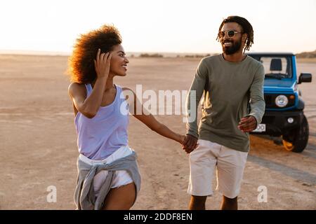 Image d'un joyeux couple afro-américain qui tient les mains ensemble et marche en voiture dans le désert Banque D'Images