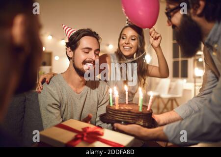 L'homme reçoit des salutations et un délicieux gâteau au chocolat avec des bougies allumées qui lui sont données par des amis. Banque D'Images