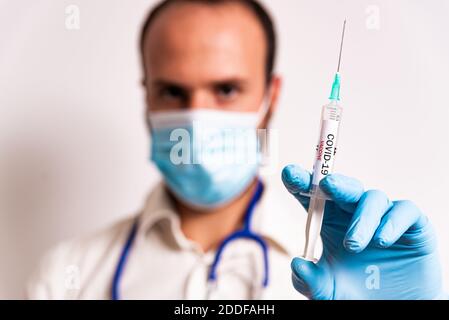 jeune homme médecin tenant une seringue de vaccin coronavirus avec un masque facial et un stéthoscope sur fond blanc. mettre fin à la pandémie par la vaccination Banque D'Images