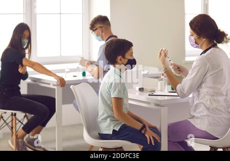 Garçon en attente de sa balle et regardant l'aiguille lorsque l'infirmière prépare le vaccin Banque D'Images