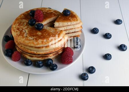 Assiette de crêpes coupée en triangle avec sirop d'érable, bleuets et framboises sur table en bois blanc et vue de dessus. Banque D'Images