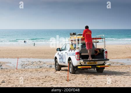 Un garde-corps RNLI debout à l'arrière d'un véhicule d'intervention d'urgence sur la plage de Fistral à Newquay, en Cornouailles Banque D'Images