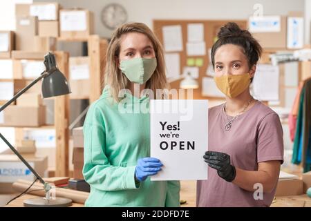 Portrait de deux jeunes femmes dans des masques de protection portant un écriteau avec le texte indiquant que le bureau est ouvert Banque D'Images