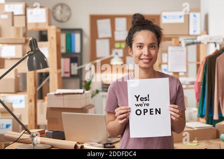 Portrait d'une jeune femme souriant à l'appareil photo tout en tenant la plaque debout au bureau Banque D'Images