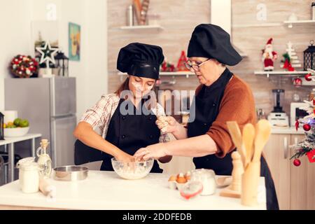 Grand-mère portant un tablier le jour de noël faisant des biscuits avec la nièce. Joyeux joyeuse adolescente aidant la femme âgée à préparer des bonbons pour célébrer les vacances d'hiver. Banque D'Images