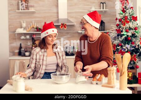 Grand-mère et petite-fille le jour de noël pâtisserie biscuits. Joyeux joyeux joyeux adolescente aidant la femme senior à préparer des biscuits doux pour célébrer les vacances d'hiver en portant le chapeau de père noël. Banque D'Images