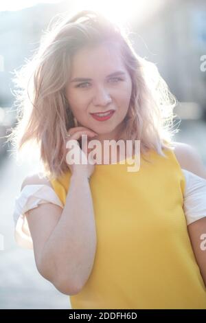 Jeune fille blonde en robe jaune posant au coucher du soleil dans une rue de Séville avec le soleil à son dos. Banque D'Images