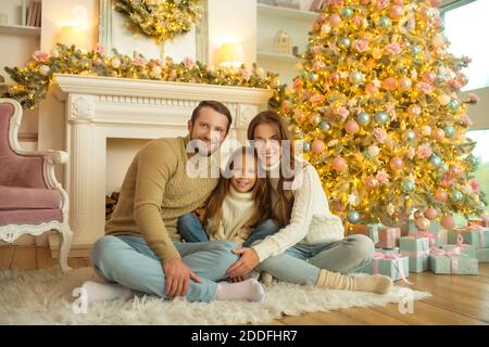 Une famille souriante et heureuse assise sur le sol près de l'arbre de noël Banque D'Images