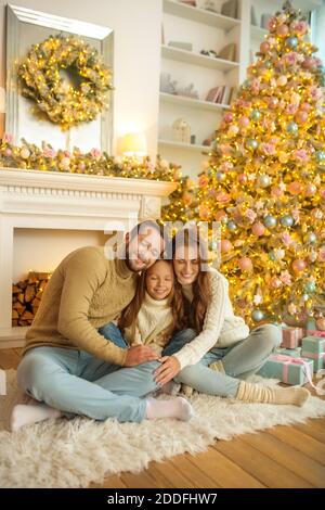 Une famille souriante et heureuse assise sur le sol près de l'arbre de noël Banque D'Images