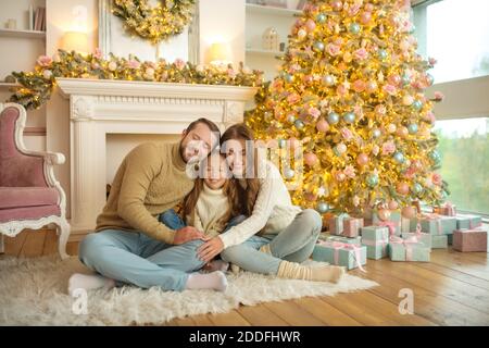 Jeune famille heureuse assise sur le sol près de l'arbre de noël et se sentir à l'aise Banque D'Images