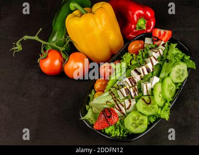 NOURRITURE - salade mixte avec fromage et fraise sur fond noir avec légumes décoratifs. Avec espace de copie Banque D'Images