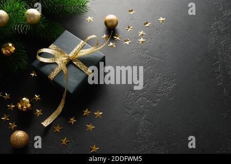 Cadeau de Noël noir avec ruban doré décoratif sur surface noire. Gros plan. Carte de vœux de Noël. Banque D'Images