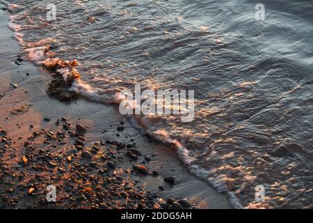 Plage de galets en gros plan avec mer de surf dans une lumière de coucher de soleil. Pierres de différentes tailles sur le fond de la mer au coucher du soleil. Banque D'Images