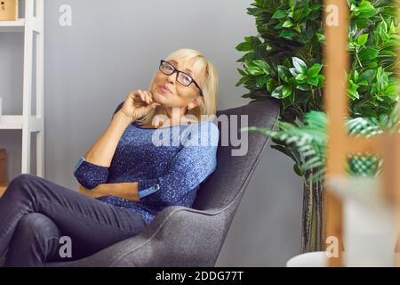 Femme mature indépendante assise dans un fauteuil à la maison, pensant et regardant la caméra Banque D'Images