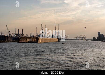 Vue sur le bord de mer d'un quai et de grues avec une montgolfière au-dessus de l'Elbe au coucher du soleil, Hambourg, Allemagne Banque D'Images