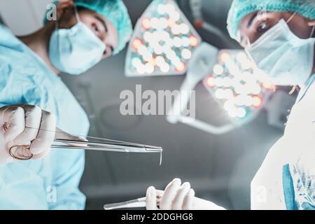 Vue latérale du dessous du chirurgien professionnel et de l'infirmière avec des ciseaux médicaux travaillant ensemble dans la salle d'opération dans moderne hôpital Banque D'Images