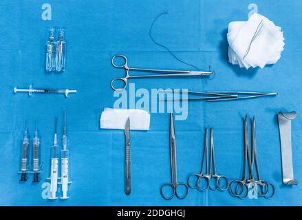 Vue de dessus de divers outils chirurgicaux en acier inoxydable et seringues médicales disposés avec des flacons et des serviettes sur fond bleu Banque D'Images