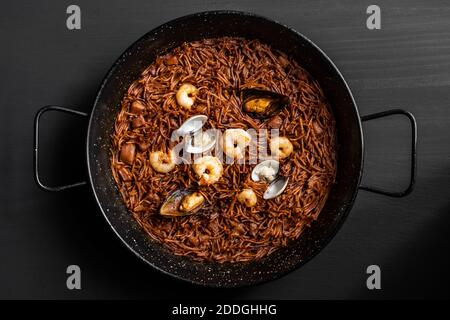 Vue de dessus de délicieux fideua avec seiches et crevettes servies dans une poêle sur une table en bois dans le restaurant Banque D'Images