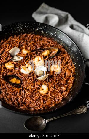 Vue de dessus de délicieux fideua avec seiches et crevettes servies dans une poêle sur une table en bois dans le restaurant Banque D'Images