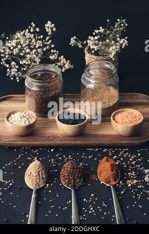 Vue de dessus de céréales variées en pots et épices aromatiques en cuillères disposées sur un plateau en bois sur une table noire Banque D'Images