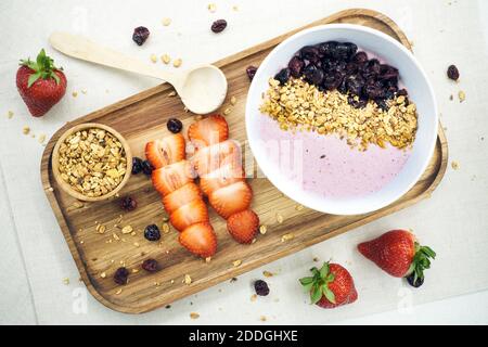 De dessus nourrissant flocons d'avoine et baies séchées dans un bol avec yaourt servi sur table avec des fraises fraîches dans la cuisine lumineuse Banque D'Images