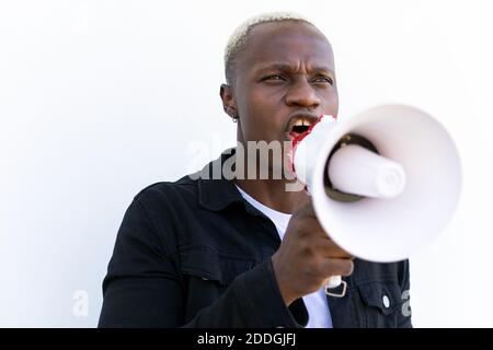 Un homme afro-américain joyeux criant dans un haut-parleur tout en restant debout arrière-plan blanc Banque D'Images
