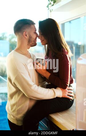 Vue latérale d'une femme sereine assise sur un comptoir dans la cuisine et embrassant avec un homme tendre Banque D'Images